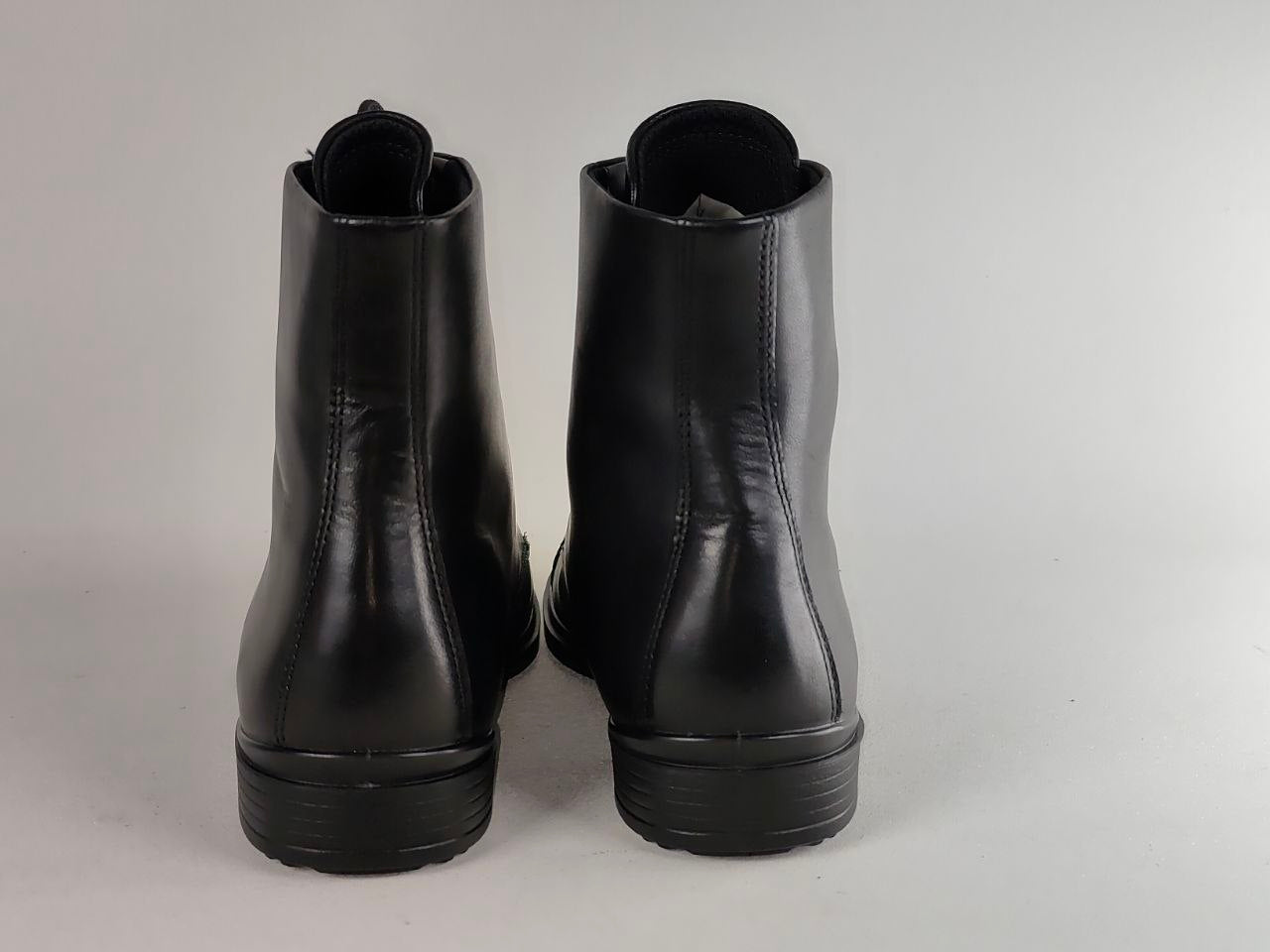 A pair of black leather ankle boots shown from the back against a light gray studio background.
