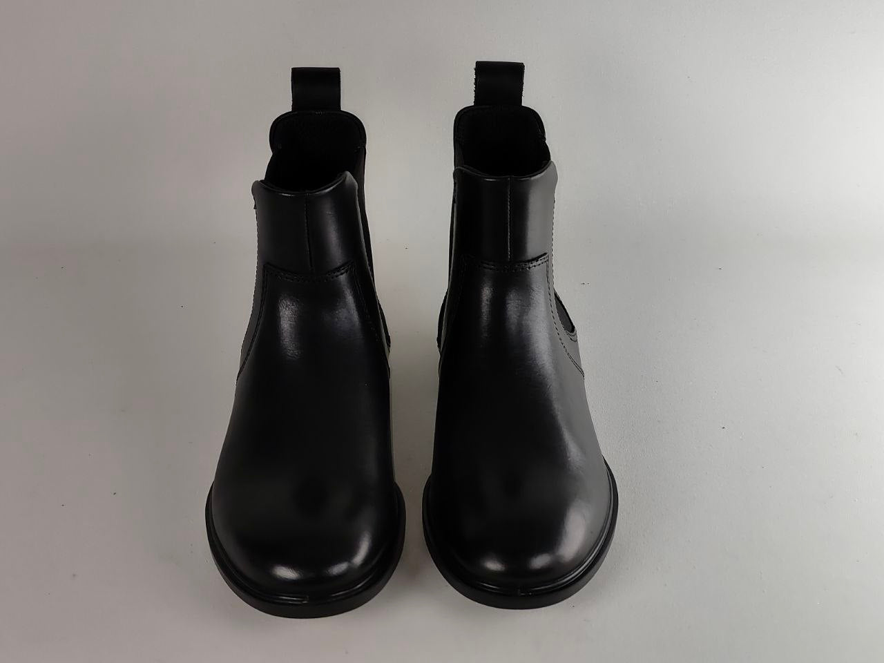 A pair of black leather Chelsea boots with elastic side gore panels and pull tabs, shown from a front-facing perspective on a light gray background.