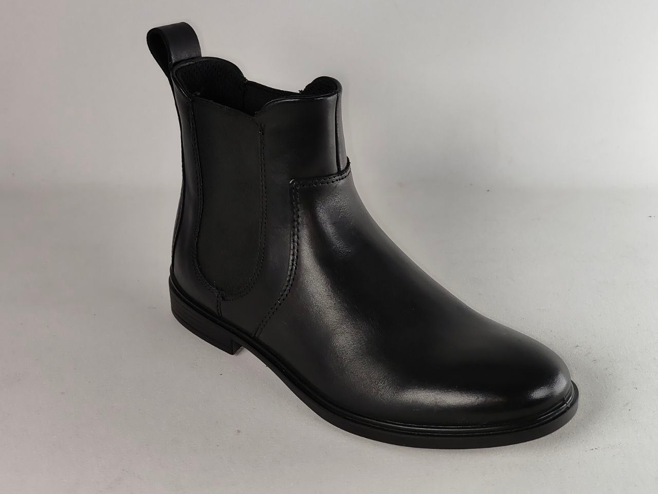 A single black leather Chelsea boot with elastic side panels and a pull tab, photographed on a light gray studio background.