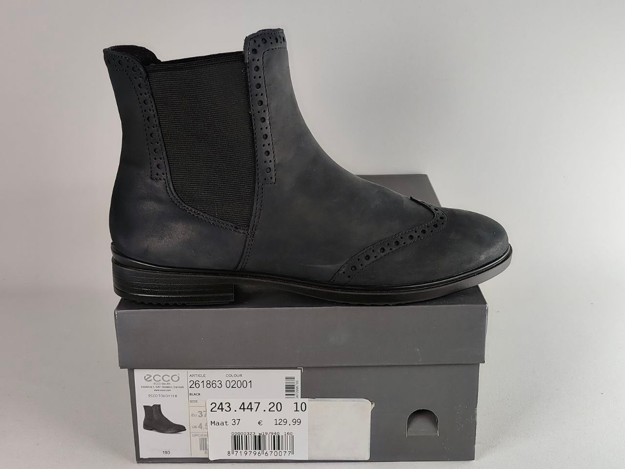 A black leather ankle boot with elastic side panels, shown in profile on top of its gray shoebox. The box features a white price and size label with the brand name 'ecco' visible.