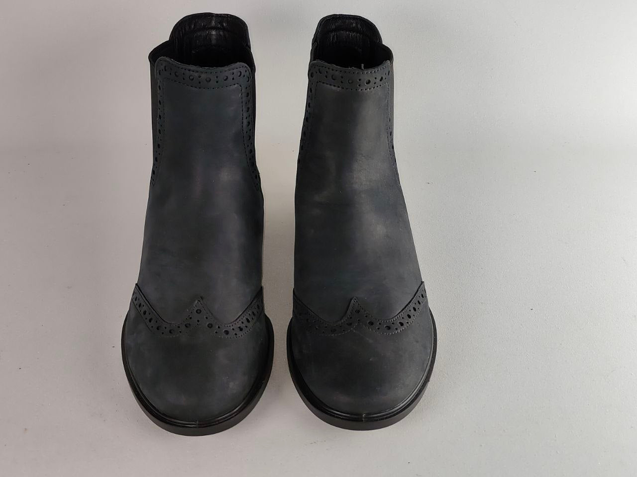 A pair of dark gray leather Chelsea boots with decorative brogue perforations on the toes, shown from a top-down view on a light gray background.