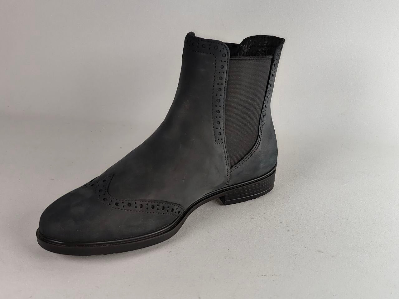A single dark gray suede Chelsea-style boot with brogue detailing on the toe and perforated side panels, photographed against a neutral light gray background.