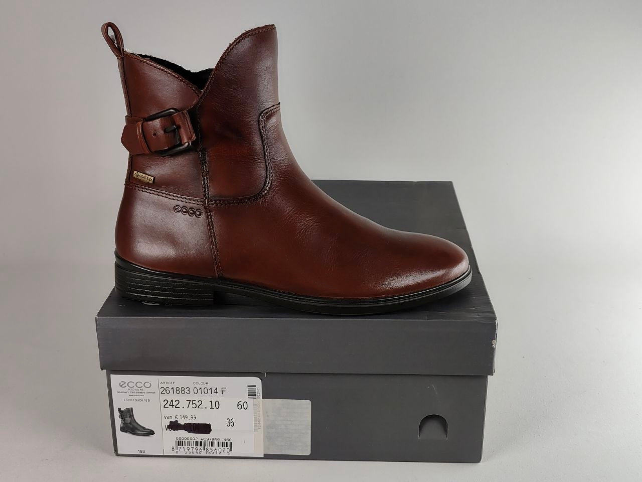 A brown leather ankle boot with a side buckle strap, displayed on top of its dark gray ECCO shoebox against a neutral gray background.