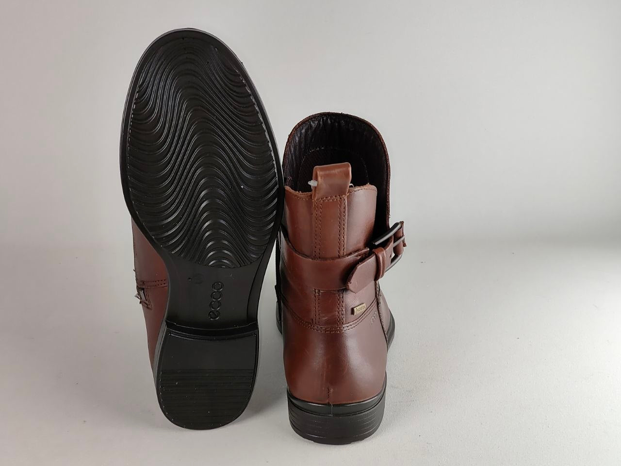 A pair of brown leather ankle boots shown from the back, displaying the brown leather side and the black treaded rubber outsole.