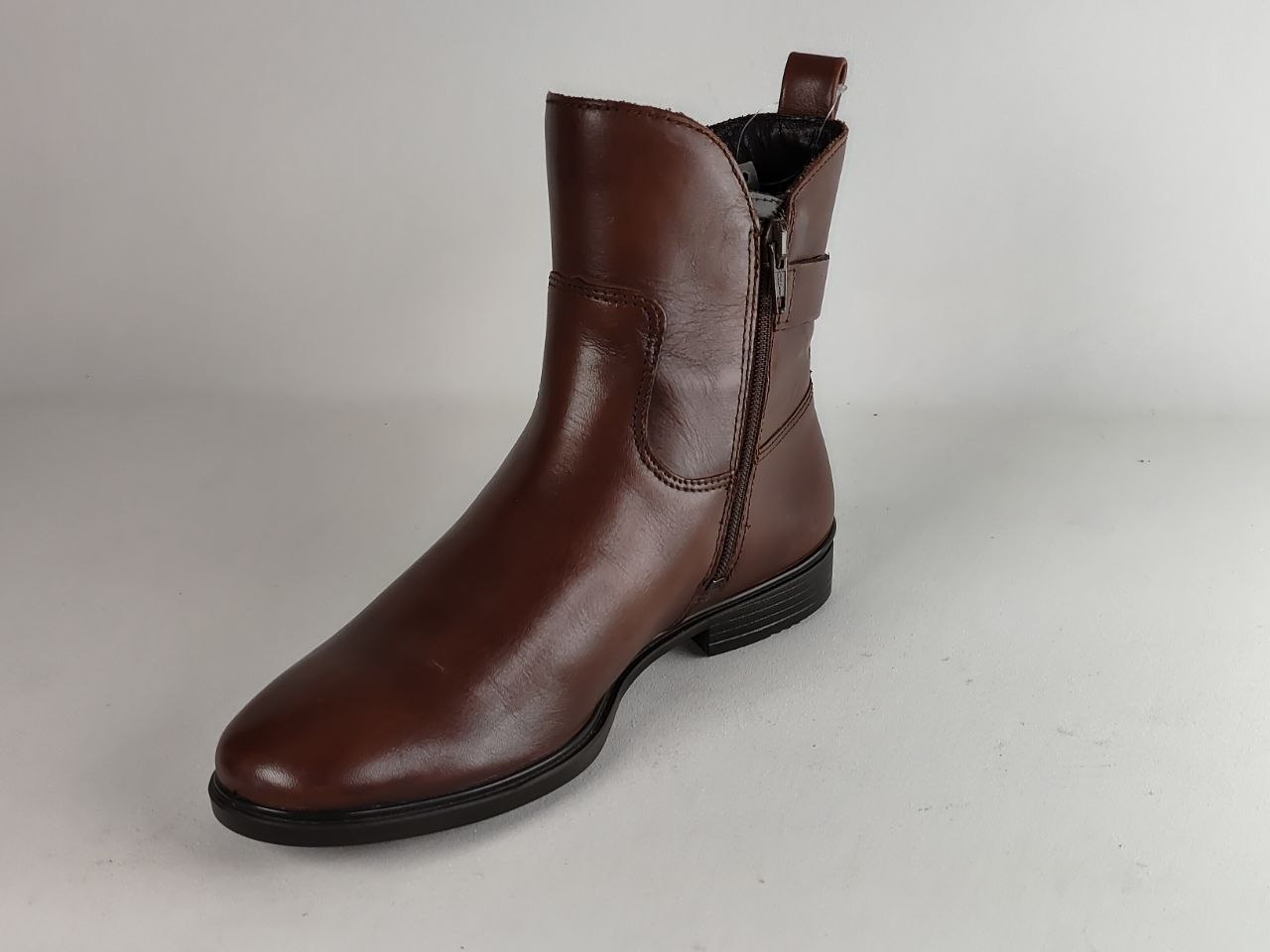 A single brown leather ankle boot with a side zipper, elastic side gore, and pull tab, shown on a neutral light gray background.