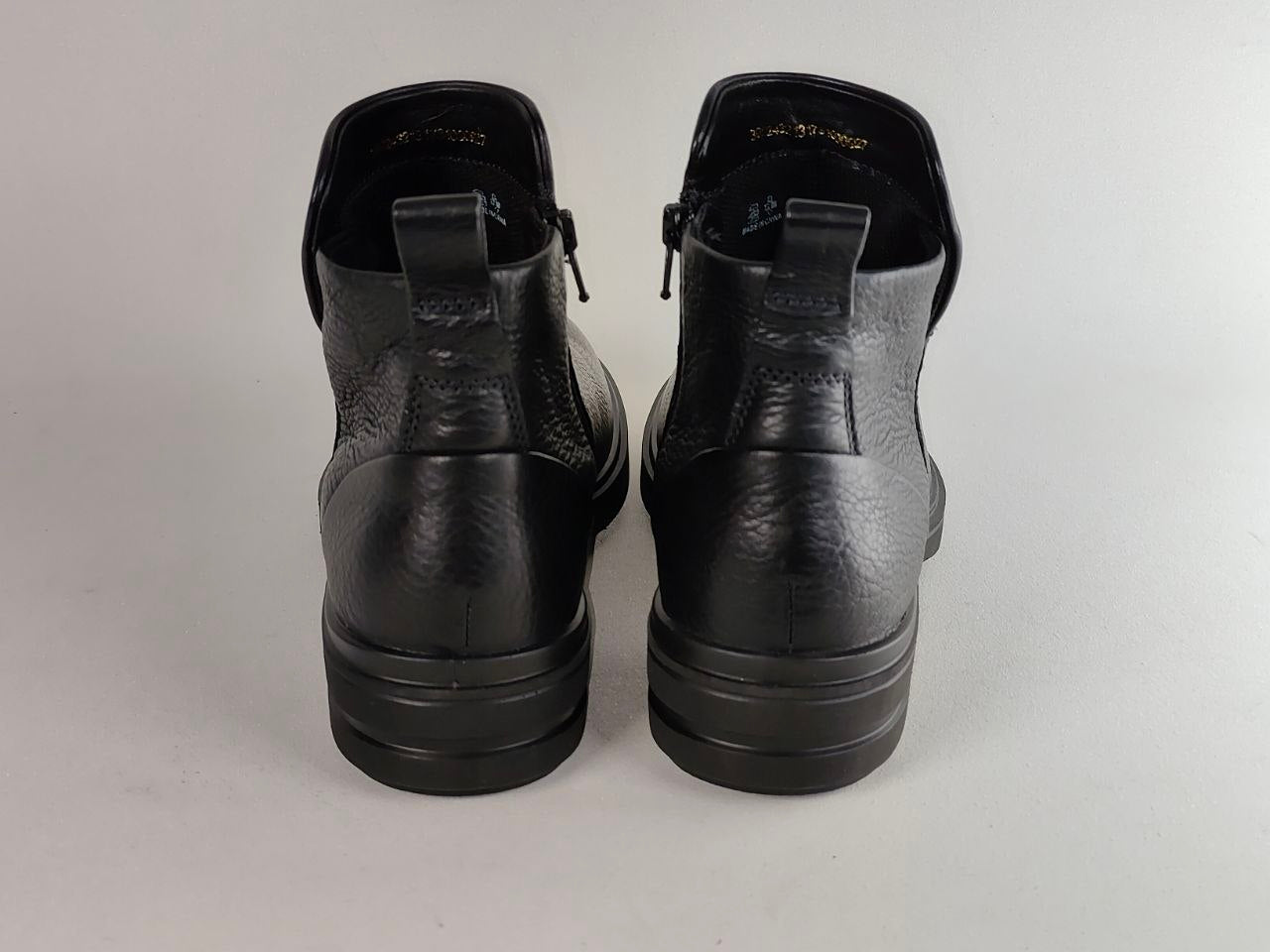 A pair of black leather ankle boots shown from the back, featuring a textured leather upper, elastic side panels, and thick black soles, set against a plain light gray background.