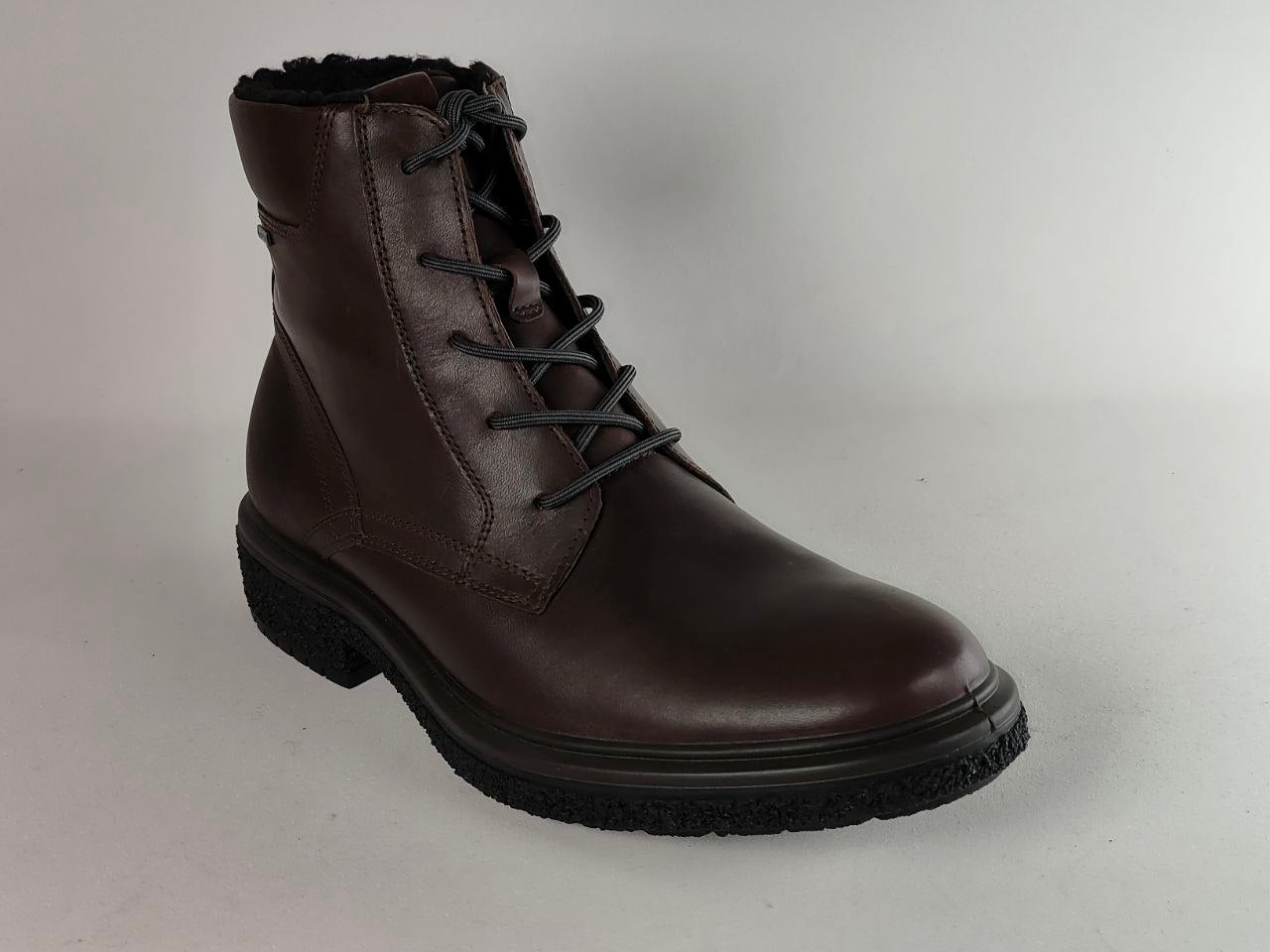 A dark brown leather lace-up ankle boot with a black sole and black laces, photographed on a light gray studio background.