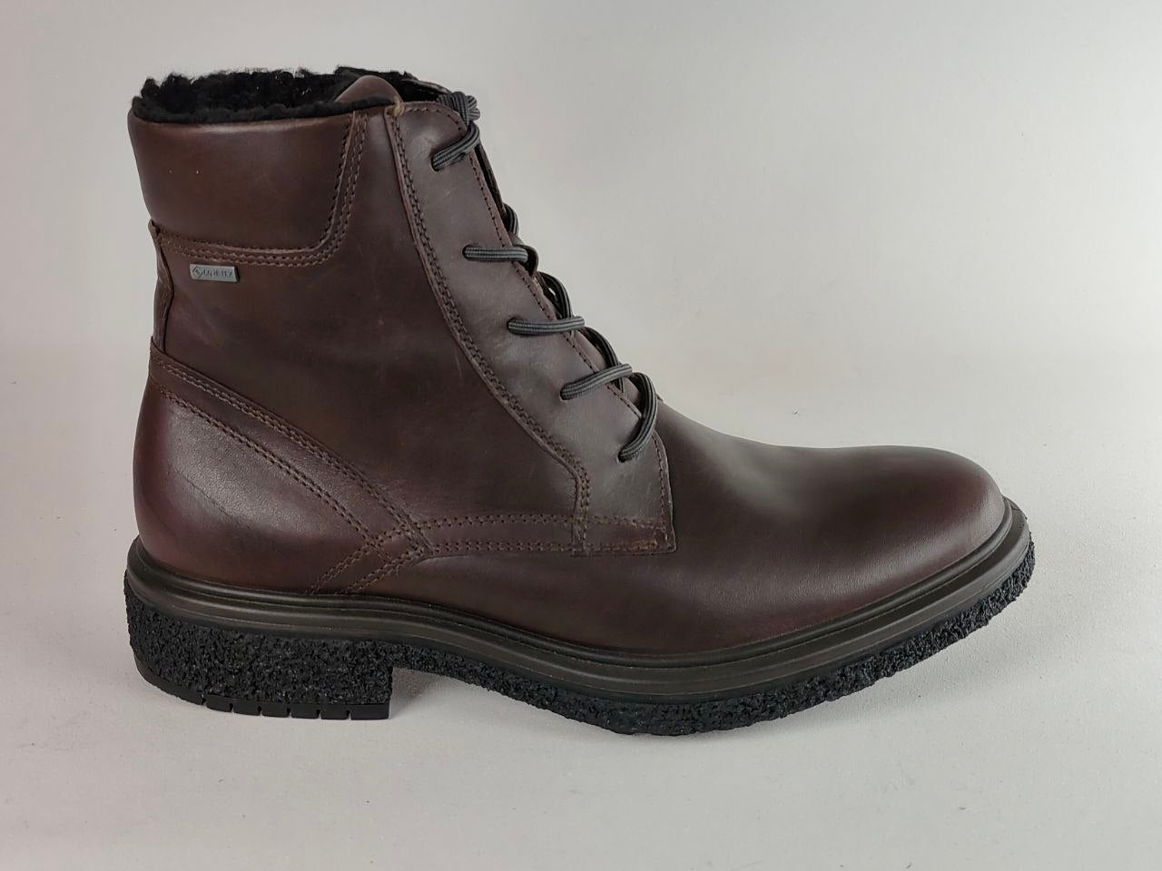 A dark brown leather lace-up ankle boot with a black textured sole and a black faux-fur lining visible at the top, shown against a light gray background.