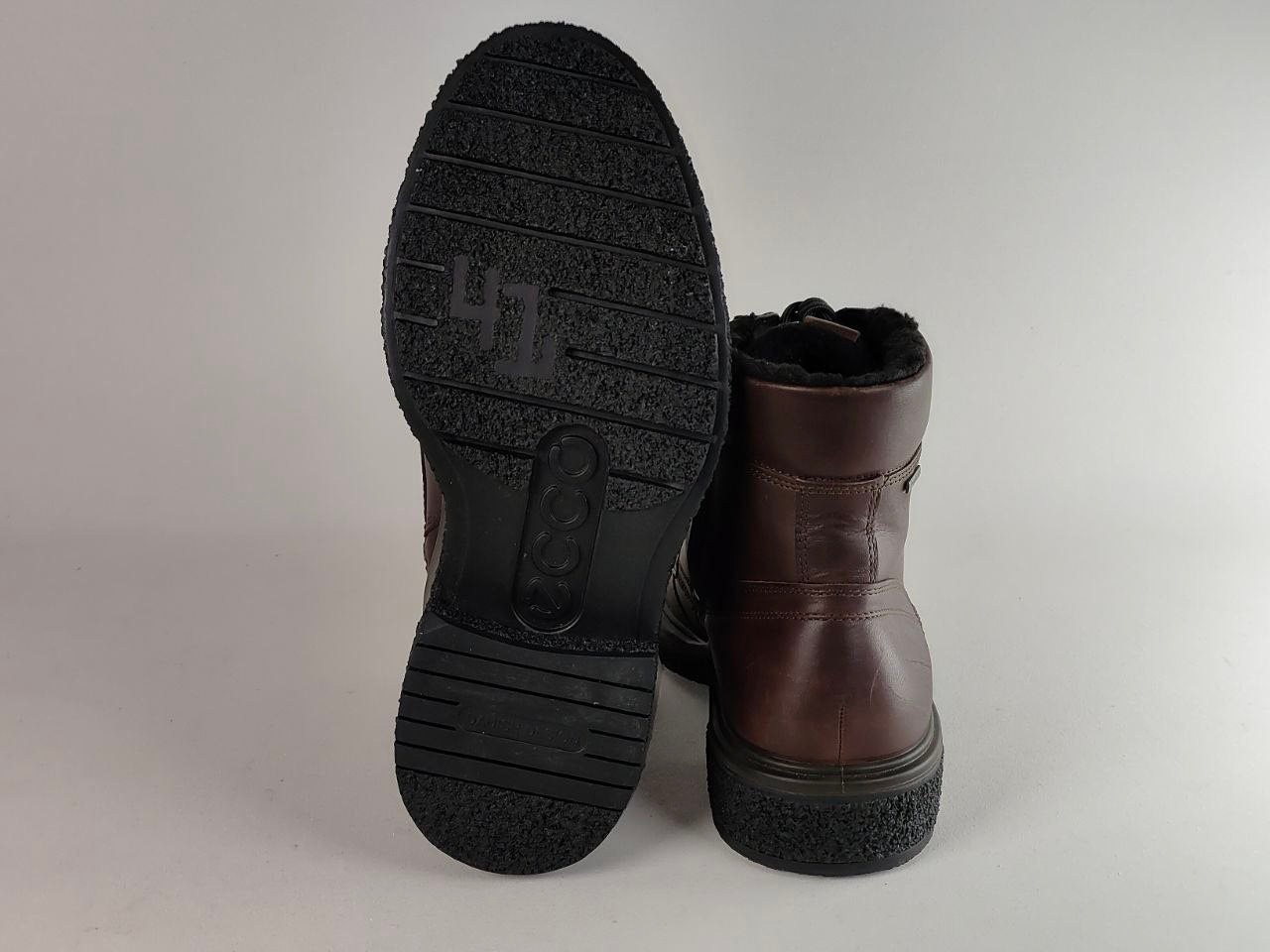 A pair of dark brown leather ankle boots with black soles, shown from the side and bottom to display the tread pattern and heel.
