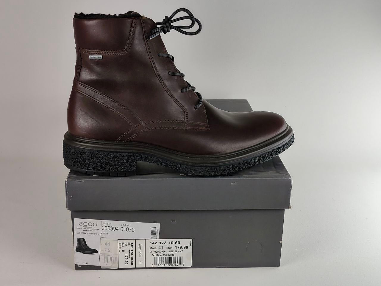 A dark brown leather lace-up ankle boot with a black sole, displayed on top of its gray ECCO shoebox against a neutral gray background.