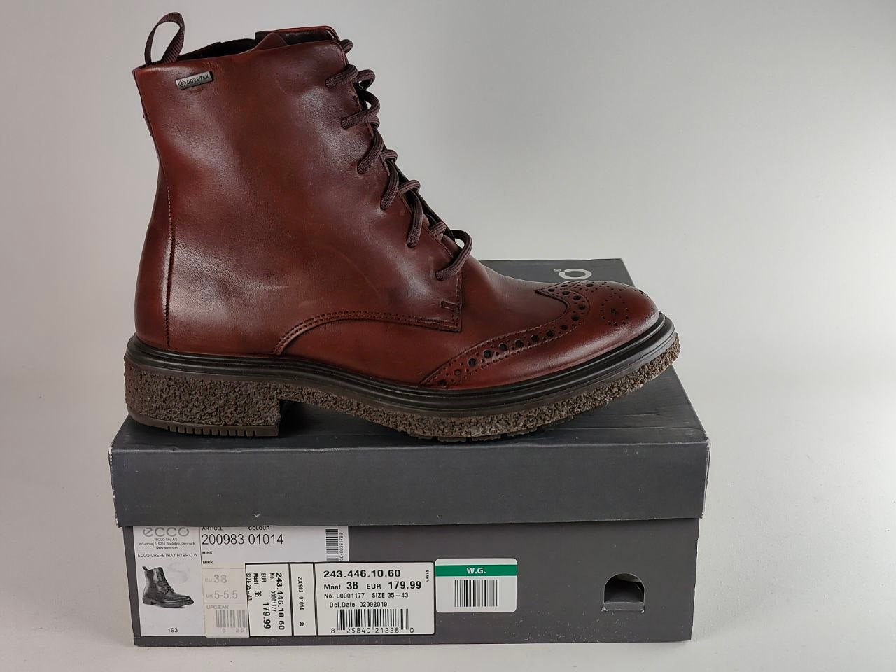 A brown leather lace-up ankle boot with brogue detailing, resting on top of its dark gray shoebox against a neutral light gray background.