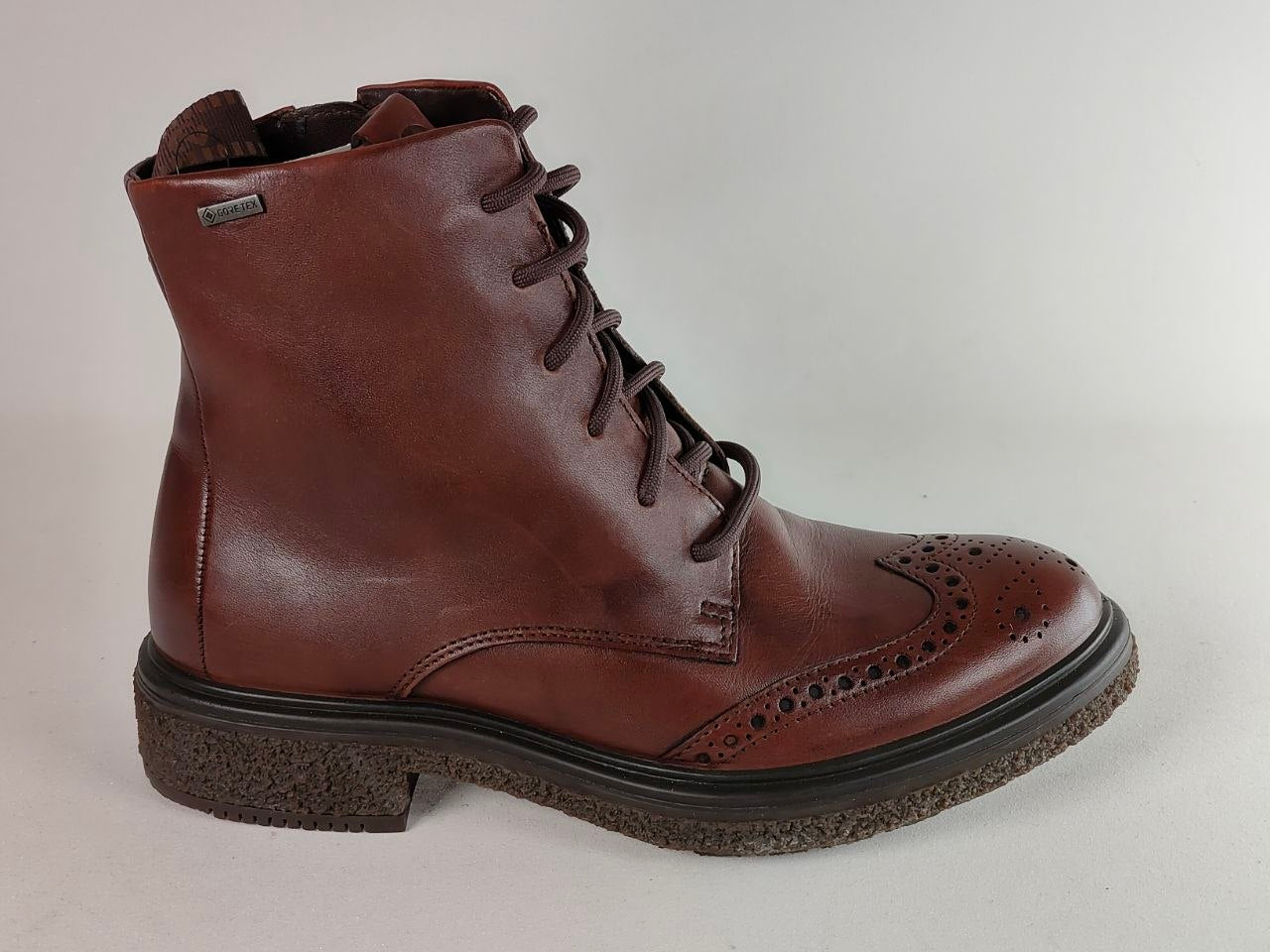 A brown leather lace-up ankle boot with brogue detailing on the toe and heel, set against a plain light gray background.