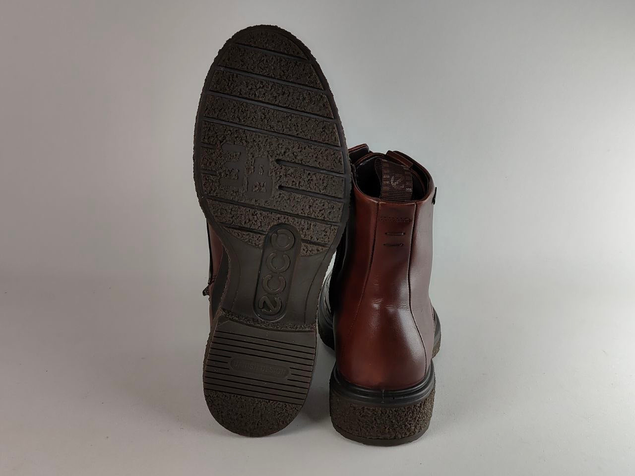 A pair of brown leather ankle boots shown from the back, with one boot displaying its textured black outsole and the other showing the side profile.