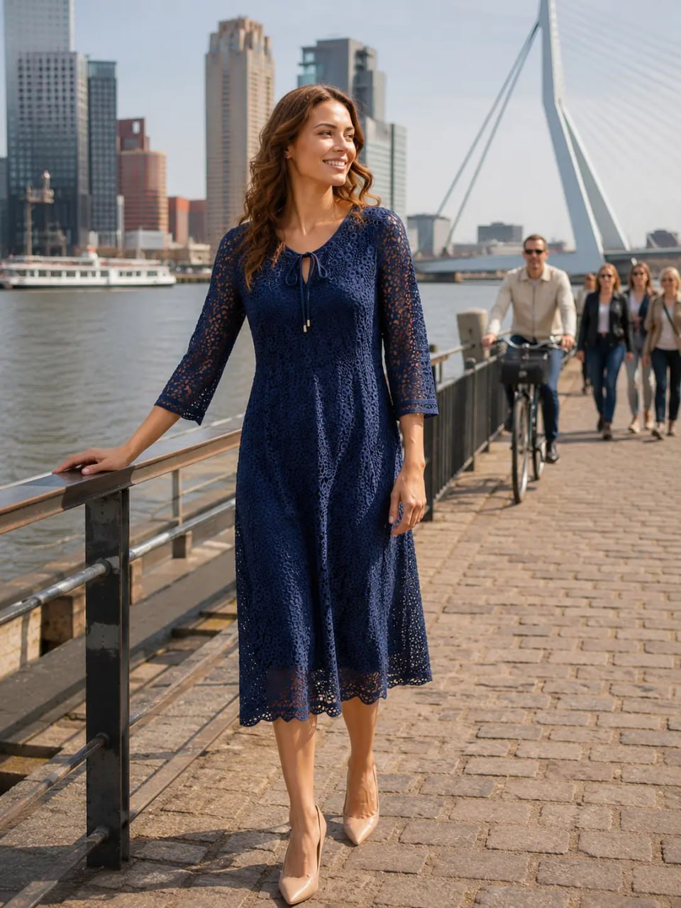 Woman in a blue dress standing by a waterfront with a city skyline in the background