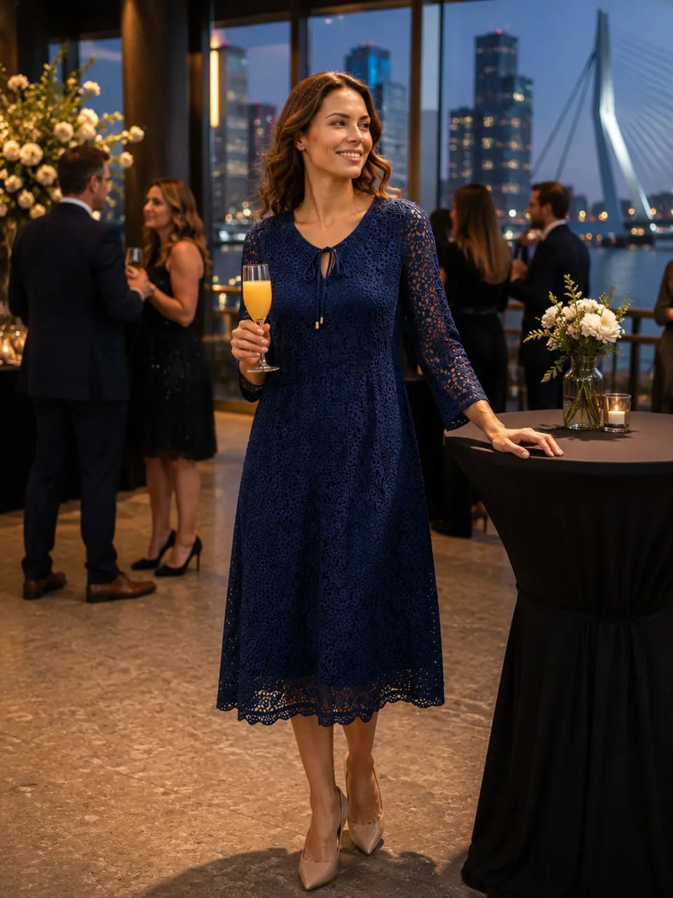 Woman in a navy lace dress holding a glass of orange juice at an evening event with cityscape background