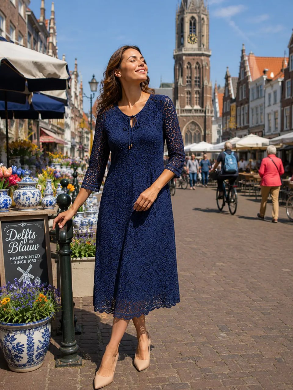 Woman in a blue dress walking through a historic town square with a clock tower.