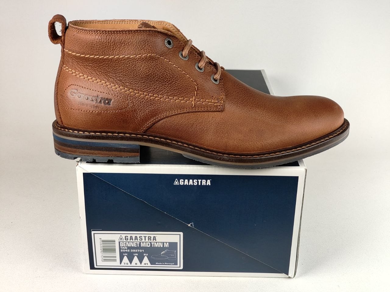 A brown leather ankle boot by Gaastra, shown in profile resting on top of its blue and white retail box against a light gray background.