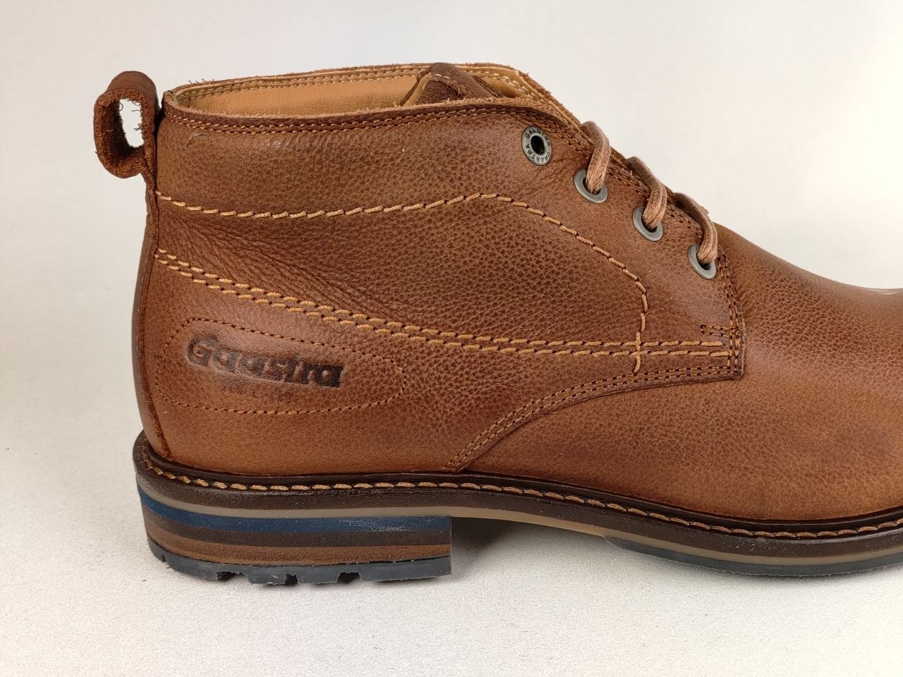 A close-up side view of a brown leather ankle boot with a pull tab, laces, and the brand name 'Goddard' embossed on the side, set against a plain light background.