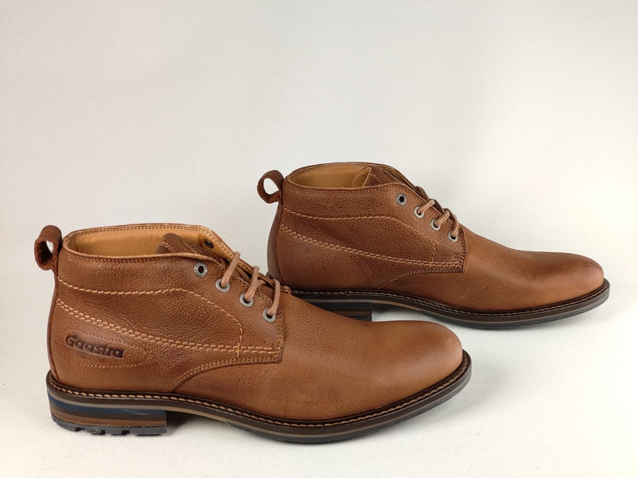 A pair of cognac brown leather lace-up ankle boots with contrast stitching and pull tabs, displayed on a light gray background.