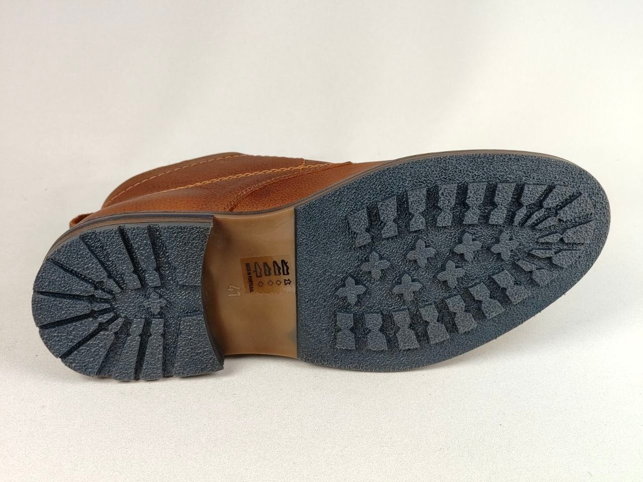 A close-up bottom view of a brown leather boot showing the dark gray textured treaded outsole and a tan insole with a visible 'COBB ELLIS' brand mark.