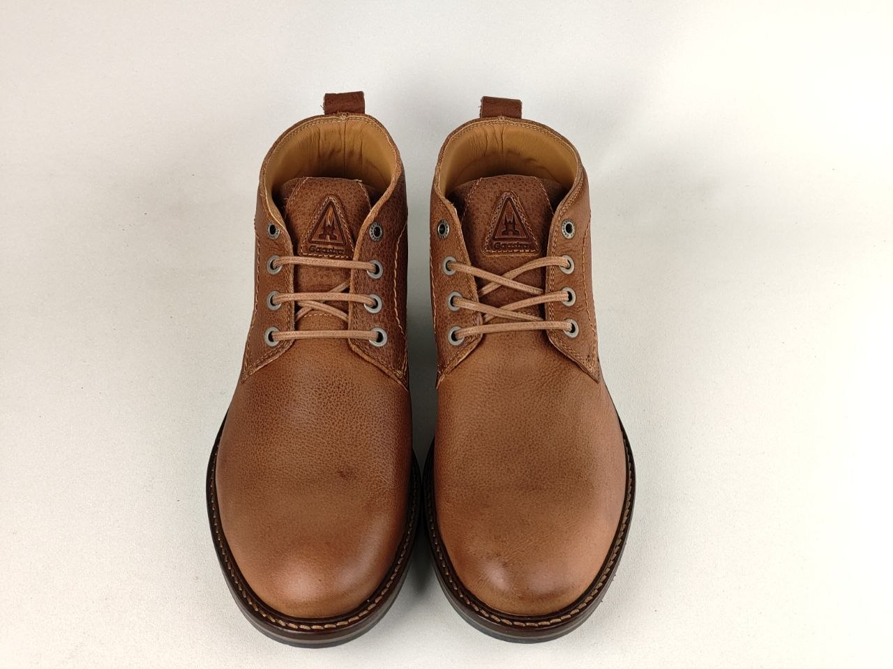 A pair of men's brown leather lace-up ankle boots with silver metal eyelets and light brown laces, shown from a top-down view on a light off-white background.
