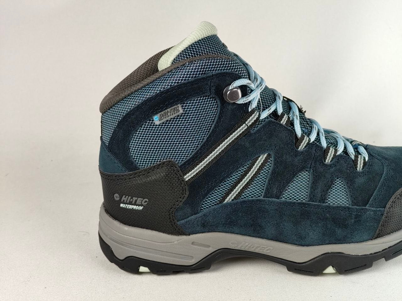 A mid-cut hiking boot in navy blue suede and mesh with light blue laces, a gray midsole, and black outsole, shown against a plain light background.