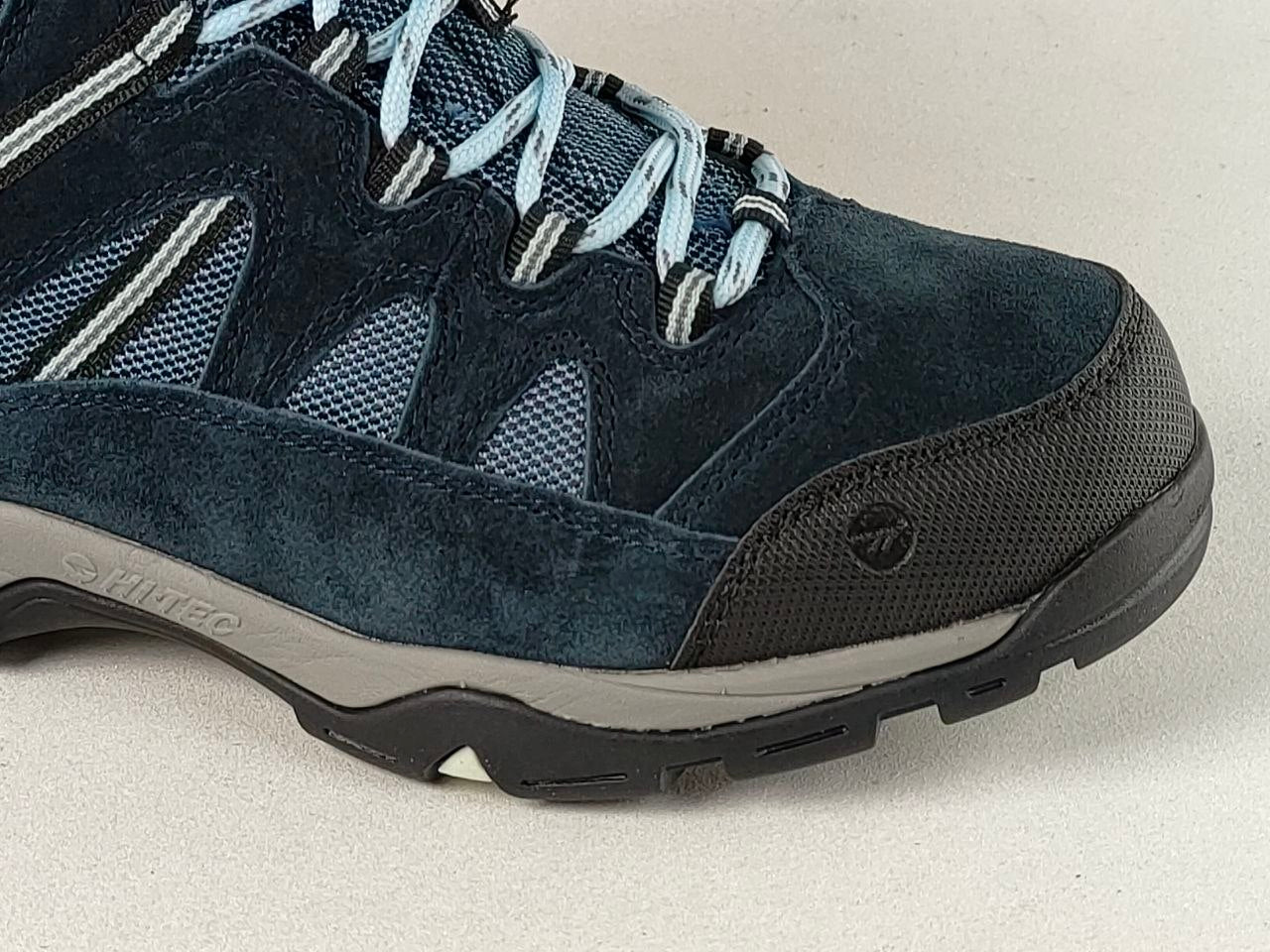 A close-up side view of a dark blue suede and mesh hiking shoe with light blue laces, a black toe cap, and a gray and black sole.