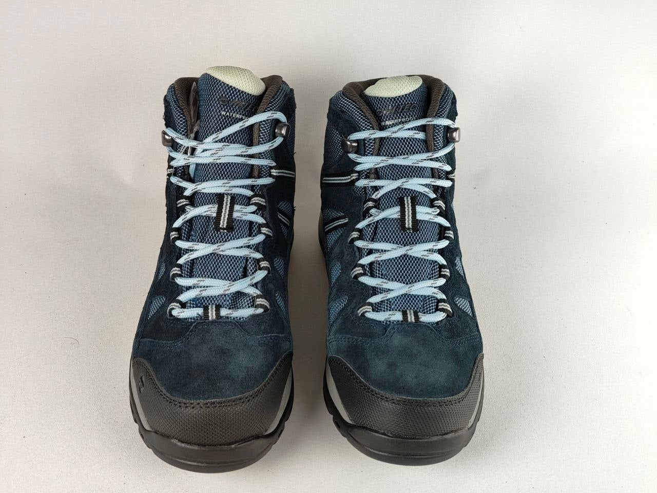 A pair of dark blue hiking boots with light blue laces and black soles, photographed against a plain off-white background.