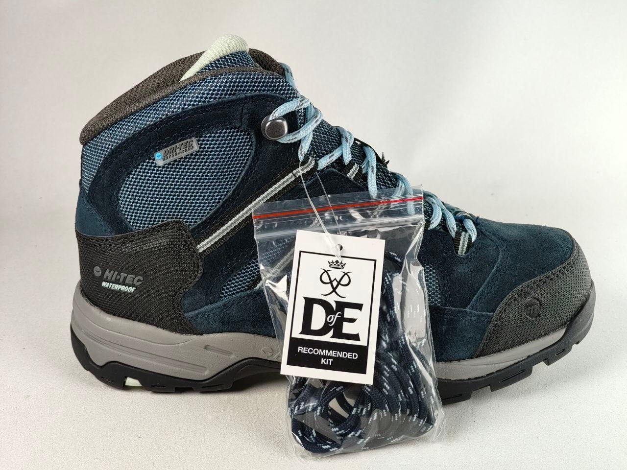A pair of blue and gray hiking boots with a pair of blue and gray laces, shown with a 'DE Recommended Kit' accessory bag in the foreground on a white background.