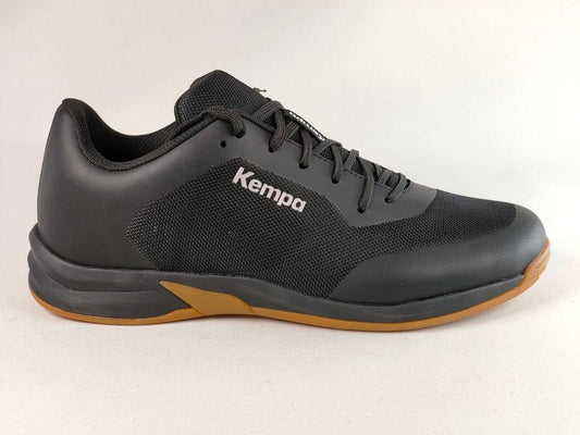 A black Kempa athletic shoe with a textured mesh upper, black laces, and a gum-colored outsole, shown from a side profile on a light gray background.