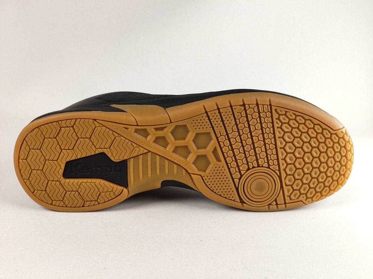 The outsole of a black and brown athletic shoe, featuring a textured gum rubber tread with a honeycomb pattern and a circular grip design.
