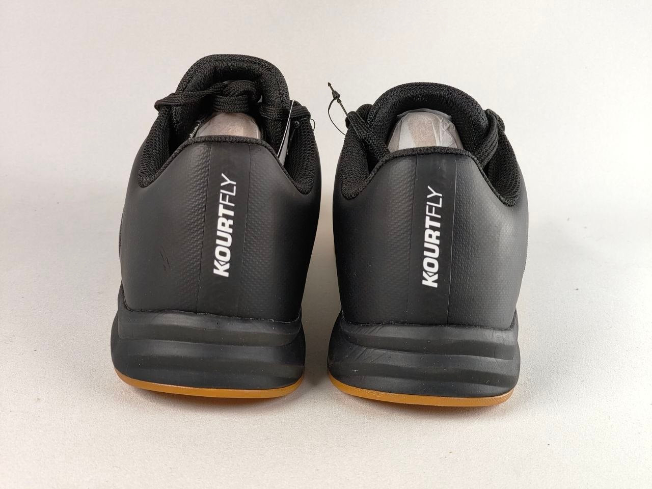 A pair of black Kourtfly athletic shoes shown from the back, featuring white vertical branding and a gum-colored outsole, set against a plain light gray background.