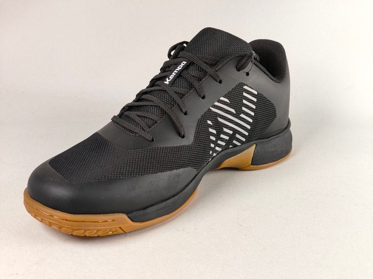 A black Kevlin indoor court shoe with a white geometric side logo and a brown gum outsole, photographed on a light gray background.