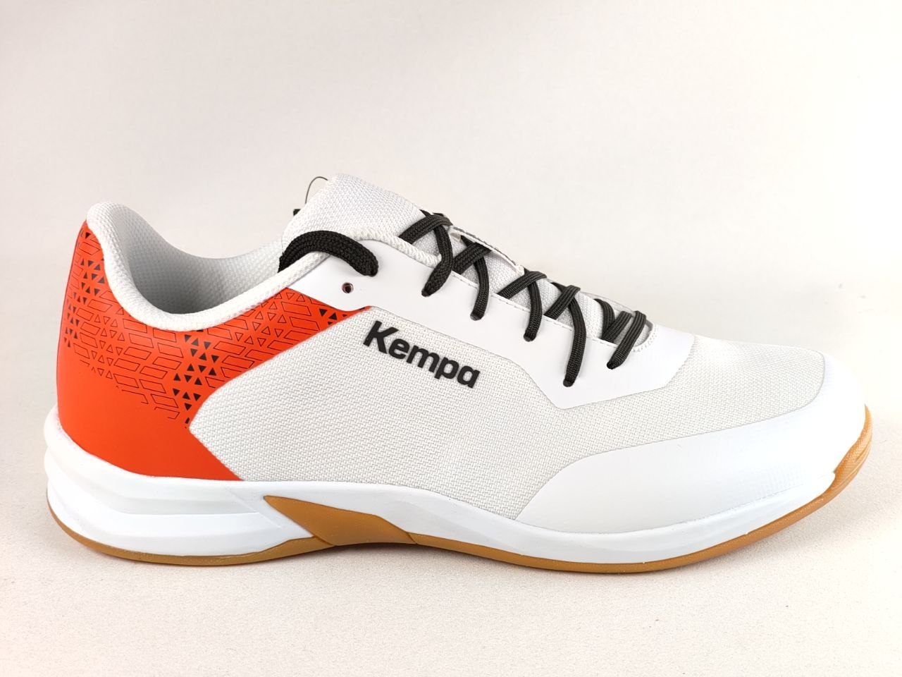 A white and orange Kempa athletic shoe with black laces and a gum outsole, shown from a side profile view against a light beige background.