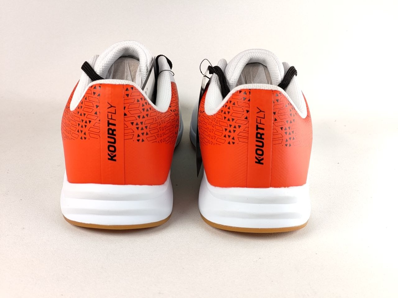 A pair of Kourt Fly athletic sneakers shown from the back, featuring a vibrant orange and white color scheme with black branding and laces, set against a plain light beige background.