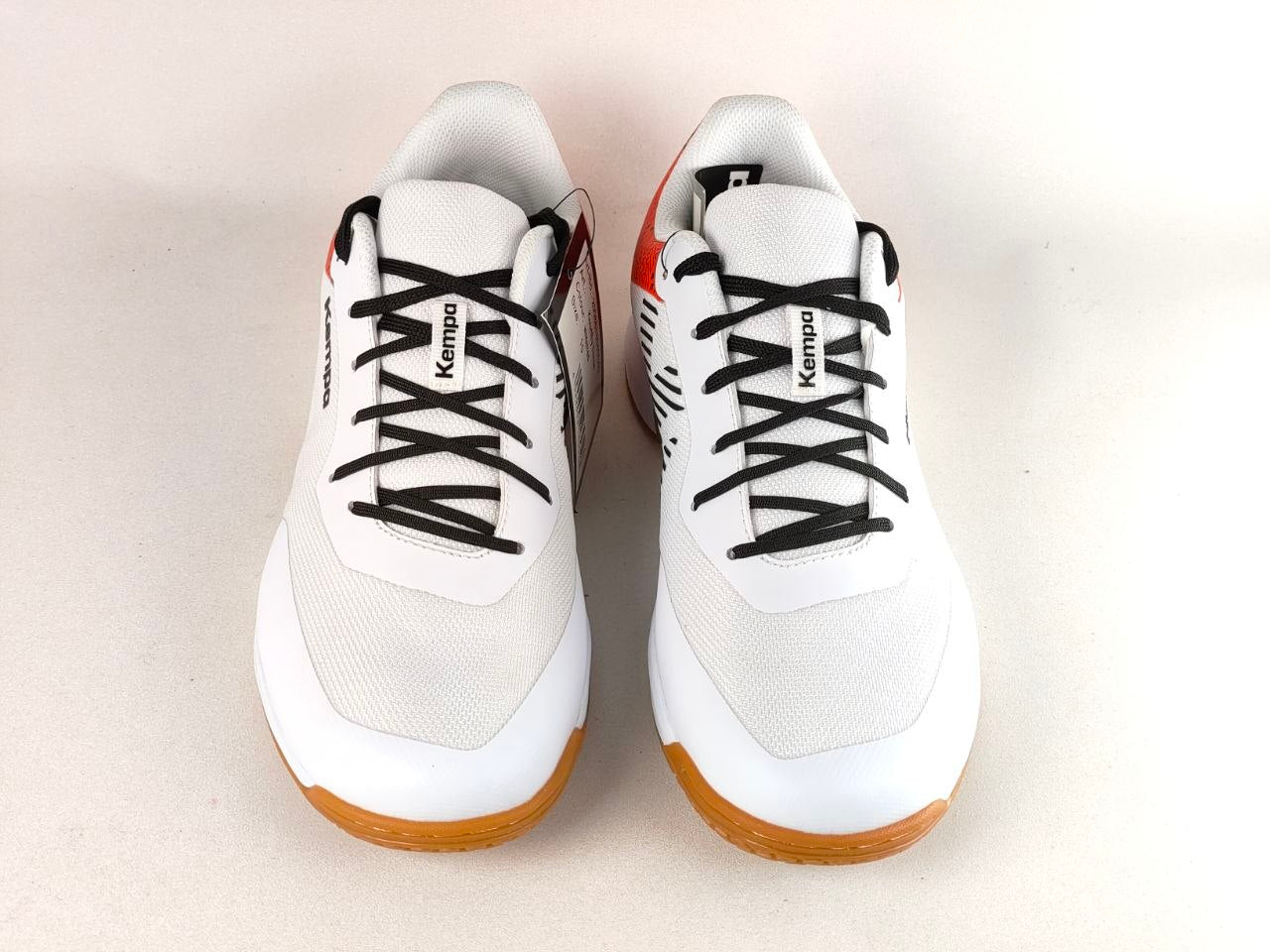 A pair of white Kempo martial arts shoes with black laces, black side stripes, and orange outsoles, shown from a top-down view on a light beige background.