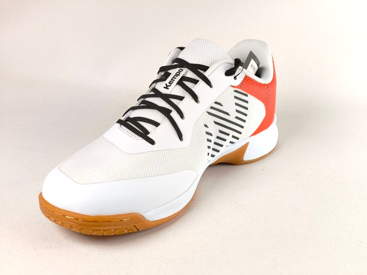 A Kevnbo indoor court shoe in white with black laces, a bright orange-red heel accent, and a gum brown outsole, shown on a light beige background.