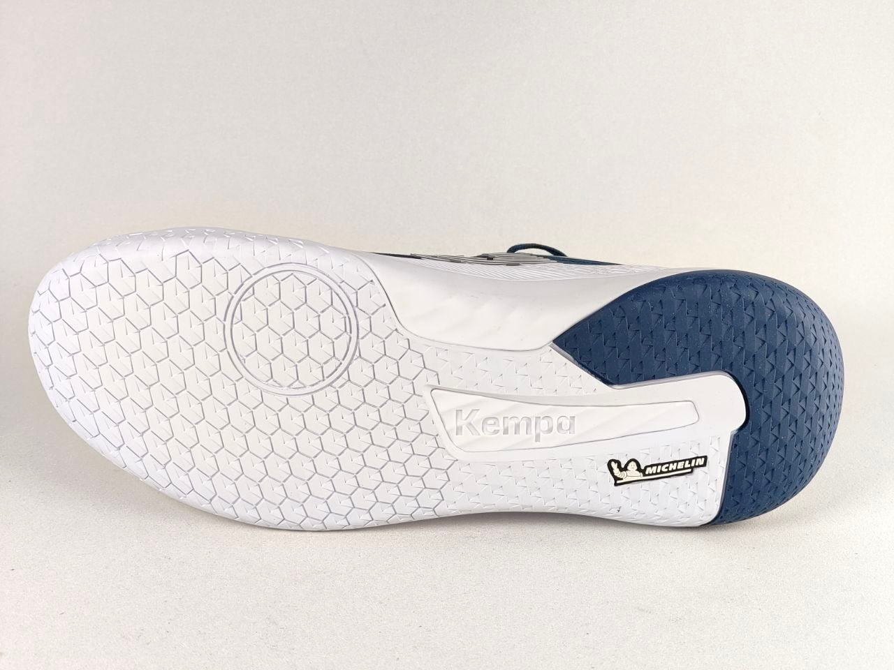 The outsole of a Kempa indoor soccer shoe, showing a white honeycomb tread pattern, a white heel section with a black Kempa logo, and a dark navy blue textured rear toe section with a black Michelin logo.