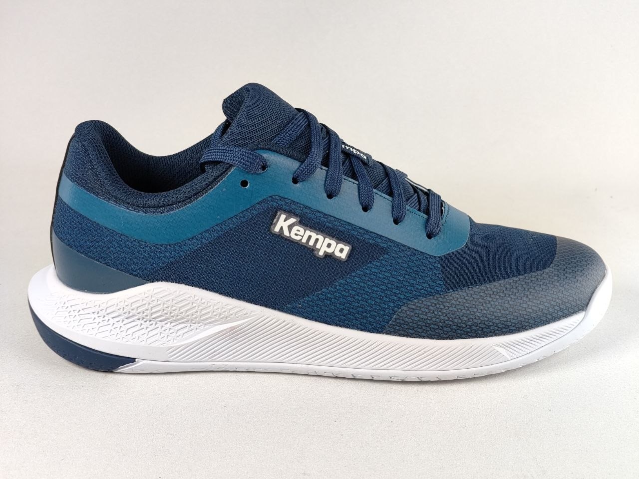 A navy blue and teal Kempa athletic sneaker with a white sole, shown from a side profile view against a light gray background.