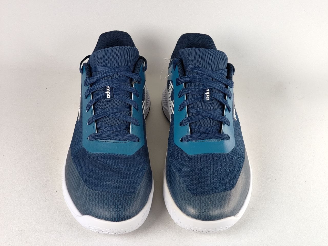 A pair of athletic sneakers in navy blue and teal with white soles, photographed from the front on a light gray background.