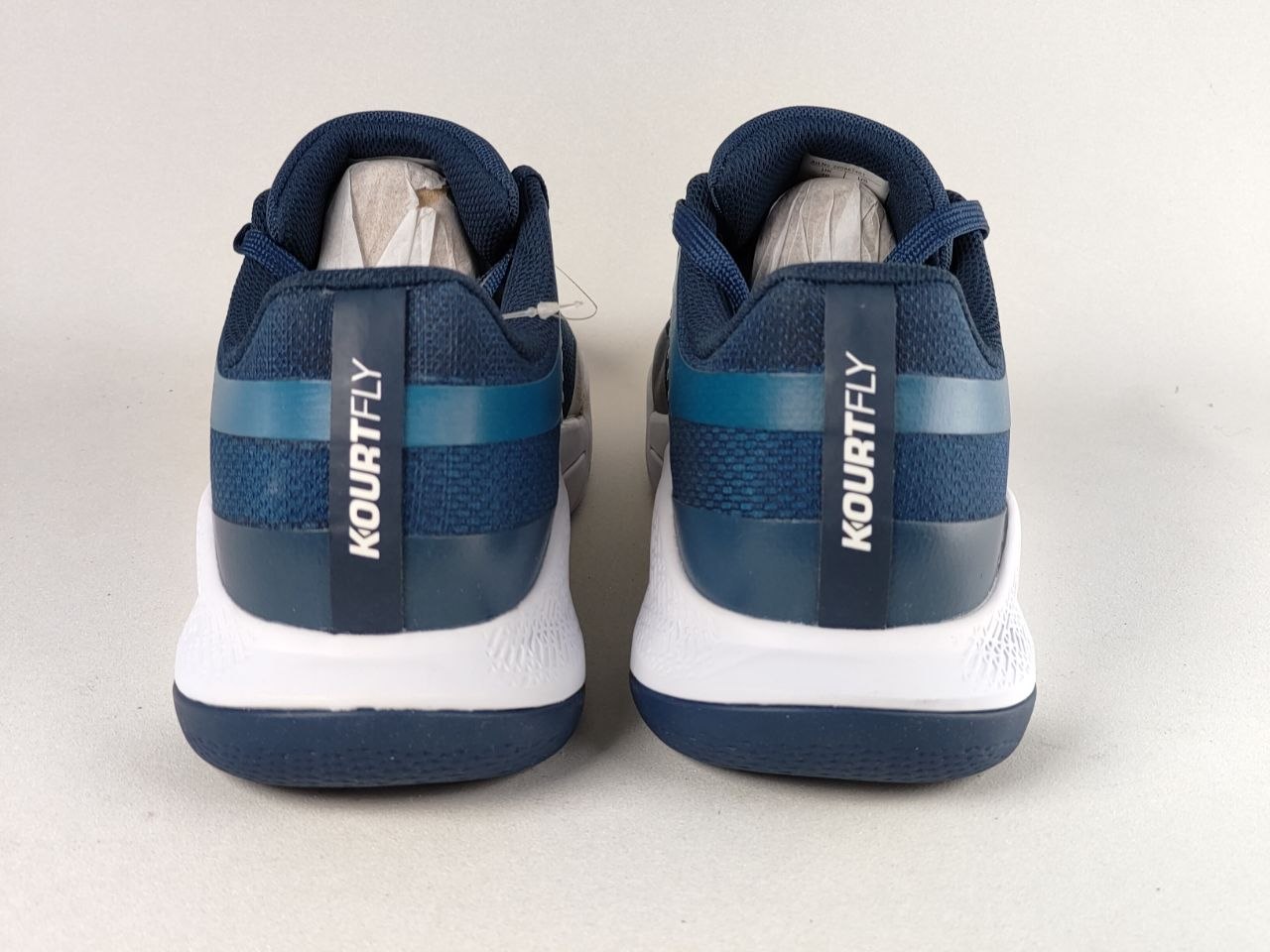 A pair of Kourt Fly athletic sneakers shown from the back, featuring a navy blue and teal mesh upper with a white midsole and dark blue outsole, set against a plain light gray background.