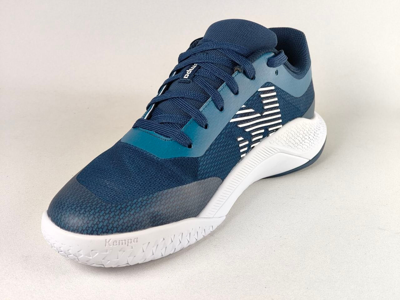A Kappa athletic shoe in navy blue and teal with a white sole, featuring a textured mesh upper and a geometric stripe pattern on the side.