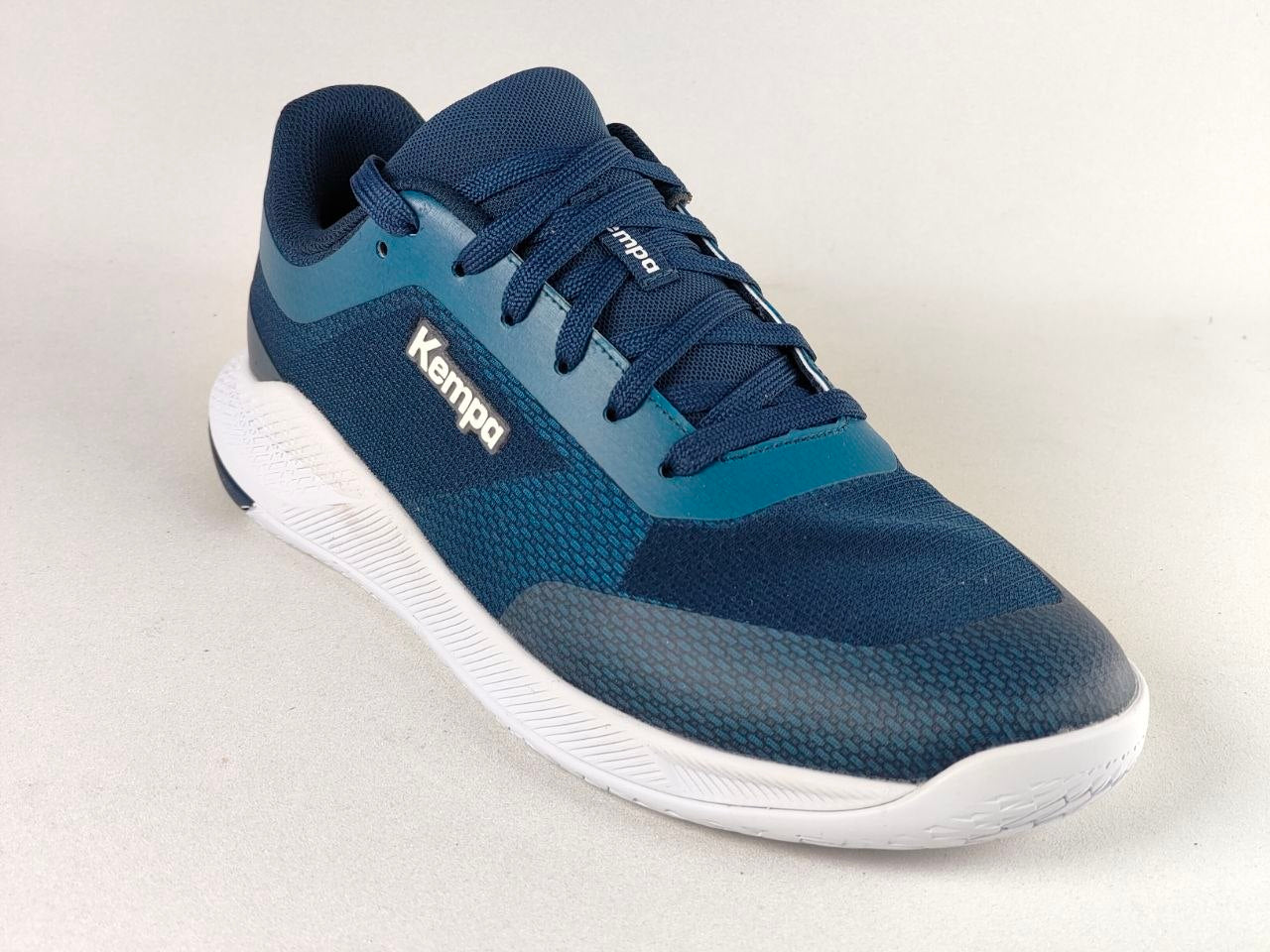 A single Kempa athletic shoe in navy blue and teal with a white sole, photographed on a light gray studio background.