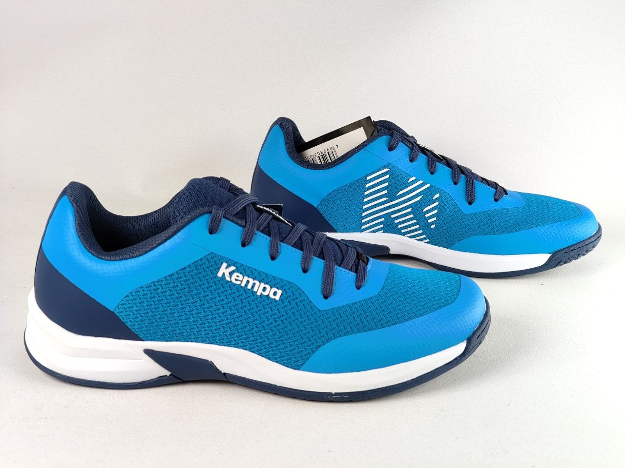 A pair of blue and navy athletic sneakers with white accents, featuring the Kempa logo on the side, displayed on a light gray background.