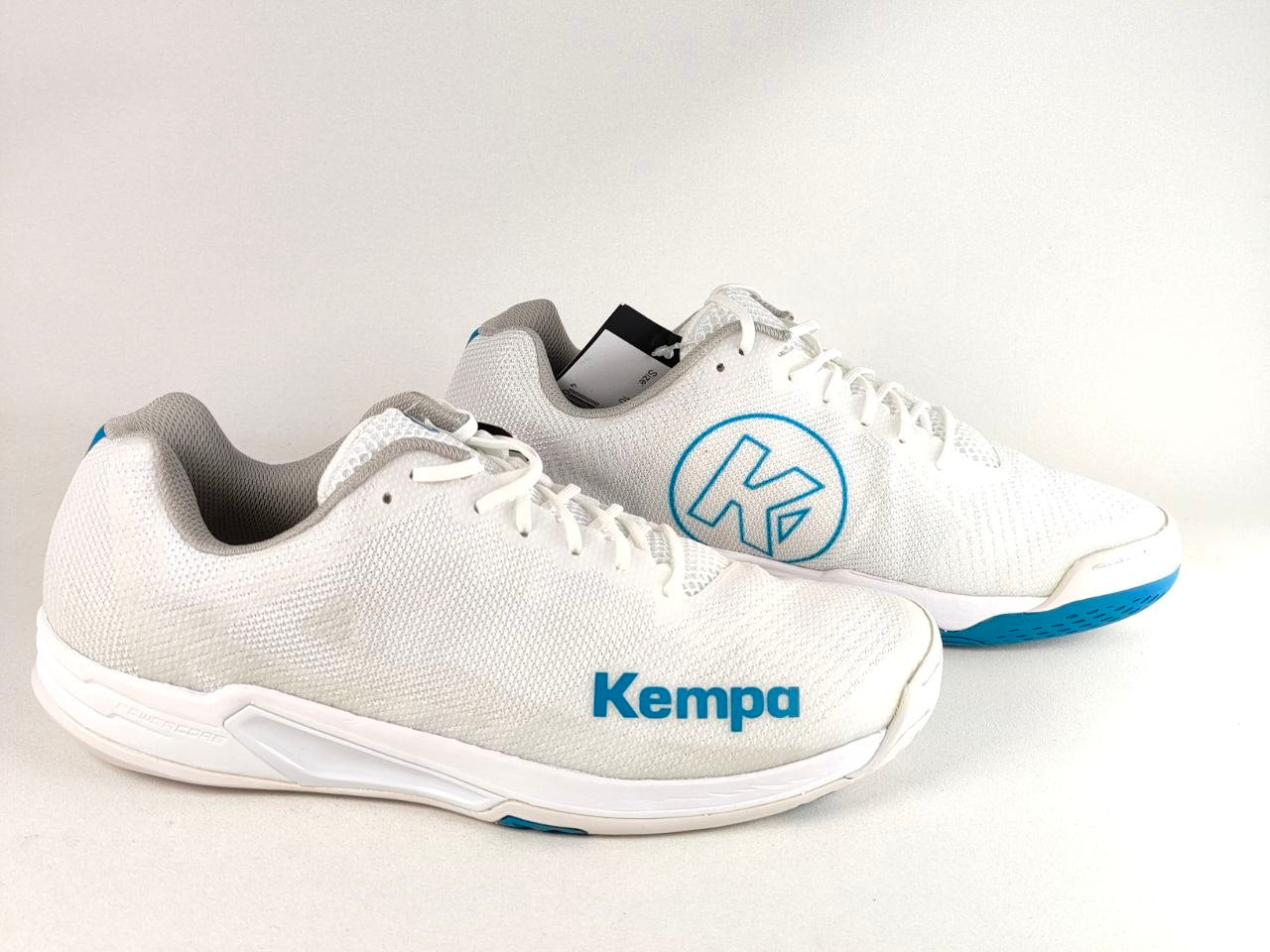 A pair of white Kempa athletic sneakers with blue accents, including a blue circular logo on the side and the blue 'Kempa' brand name on the front, set against a plain light background.