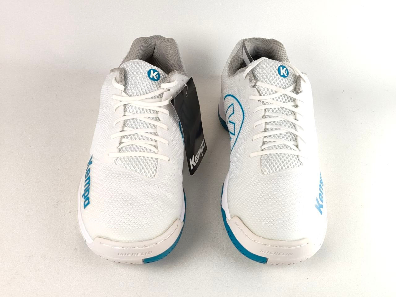 A pair of white Kermad sports shoes with blue accents and a black hangtag, photographed on a light gray background.