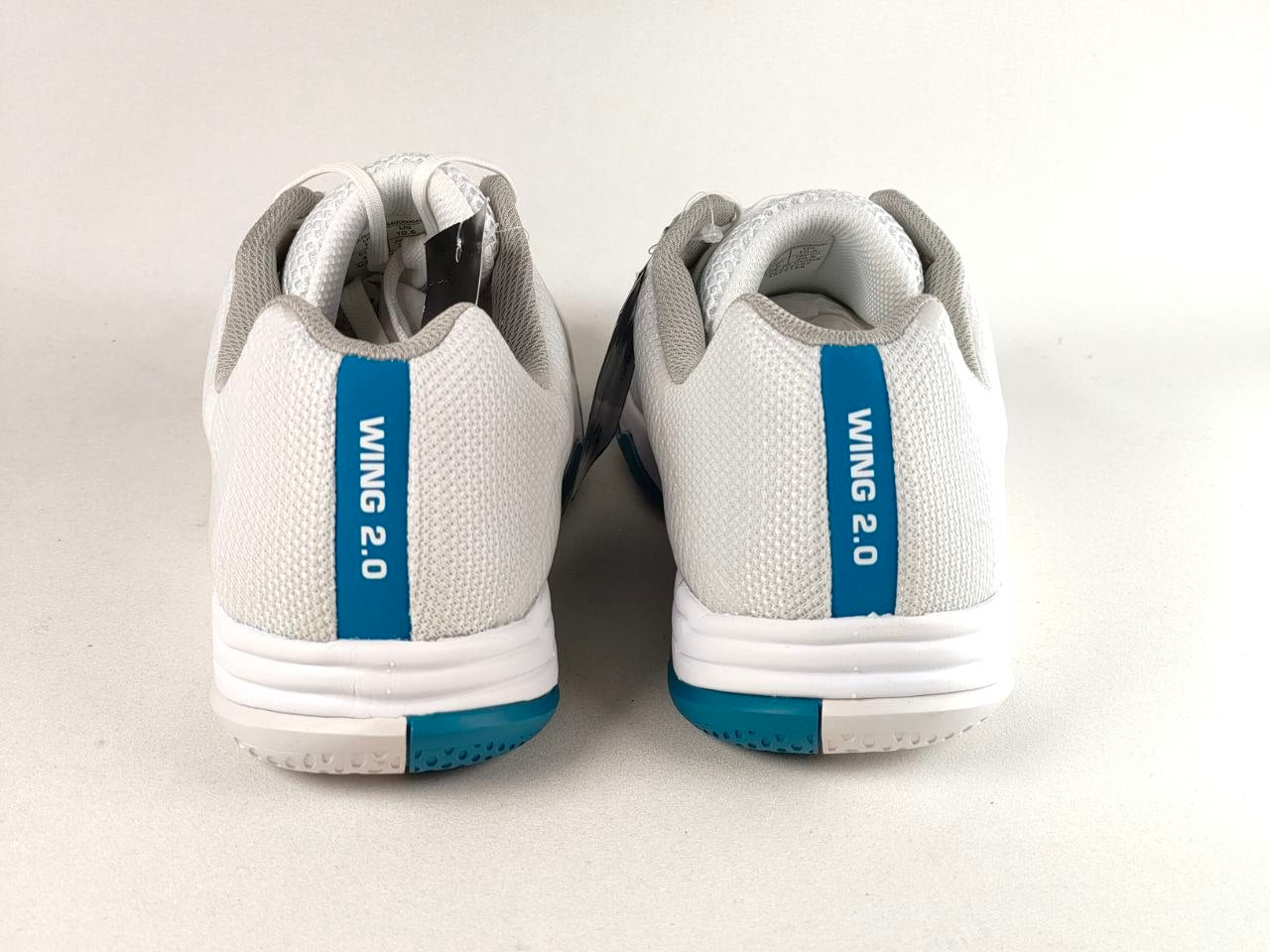 A pair of white Wing 2.0 athletic shoes shown from the back, featuring a vertical blue stripe with white text and a teal outsole accent, set against a plain light background.