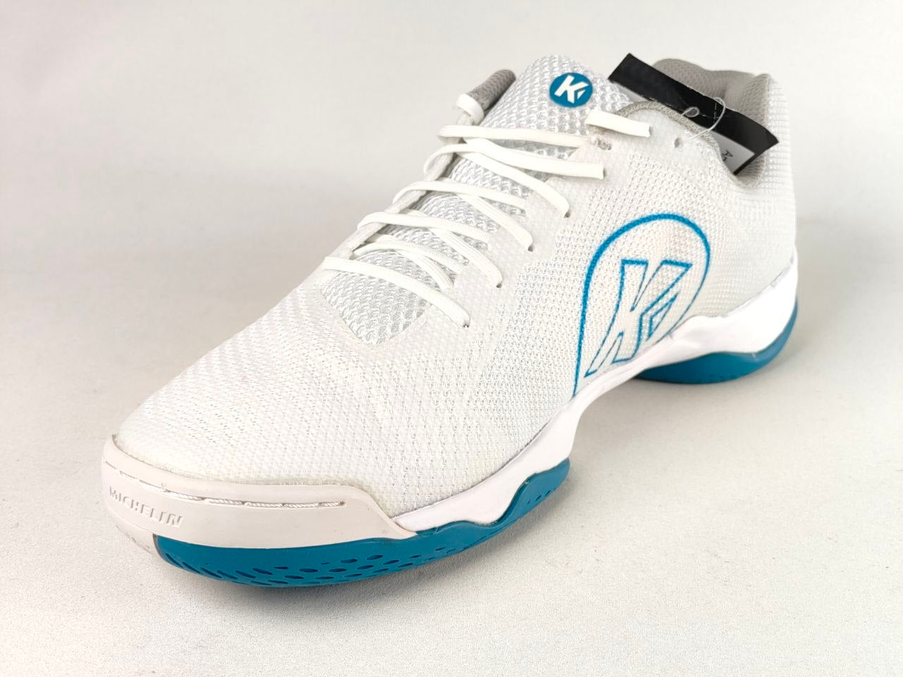 A white athletic shoe with a white mesh upper, white laces, a blue outlined logo on the side, and a blue outsole, shown on a light gray background.