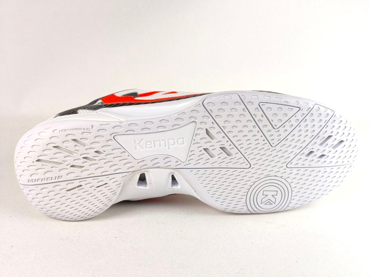 The white outsole of a Kempo brand athletic shoe, showing the textured tread pattern and brand name embossed in the center, with a hint of red and black detailing on the upper.