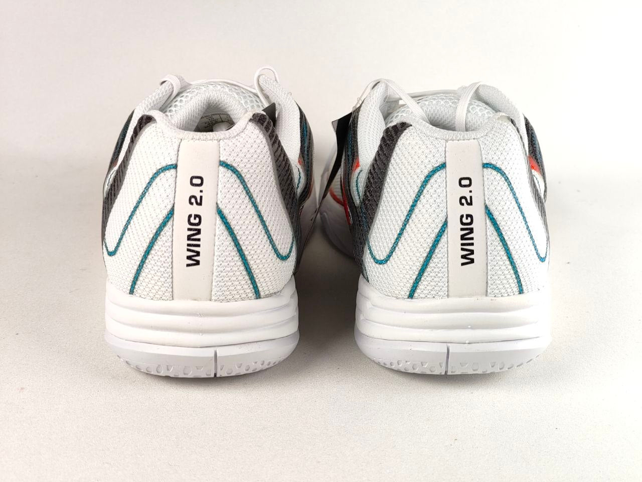 A pair of white Wing 2.0 athletic shoes shown from the back, featuring white mesh uppers with teal wave accents, a white heel tab printed with 'WING 2.